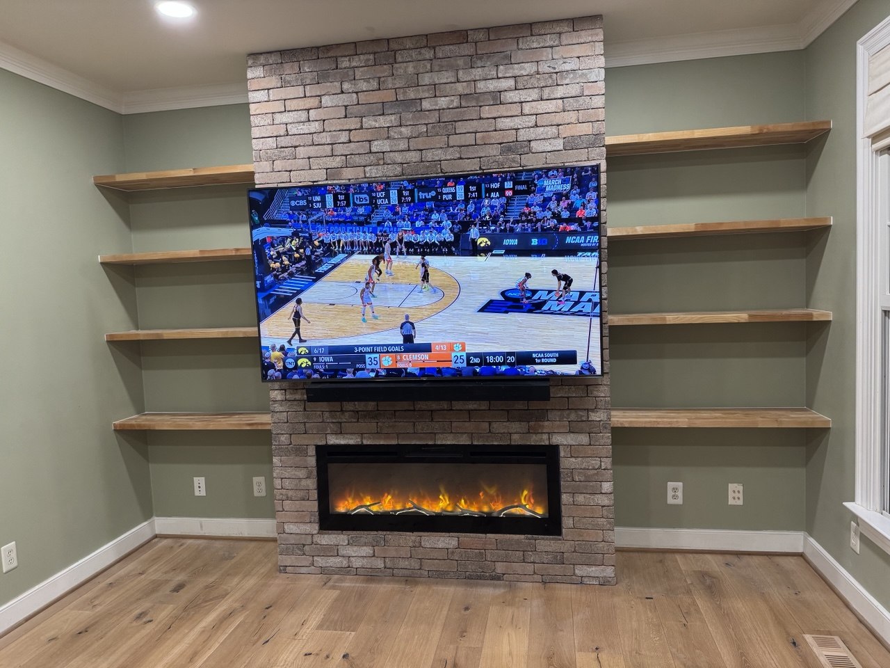 Custom feature wall with brick fireplace surround, floating wood shelves, and mounted TV in Triangle NC living room