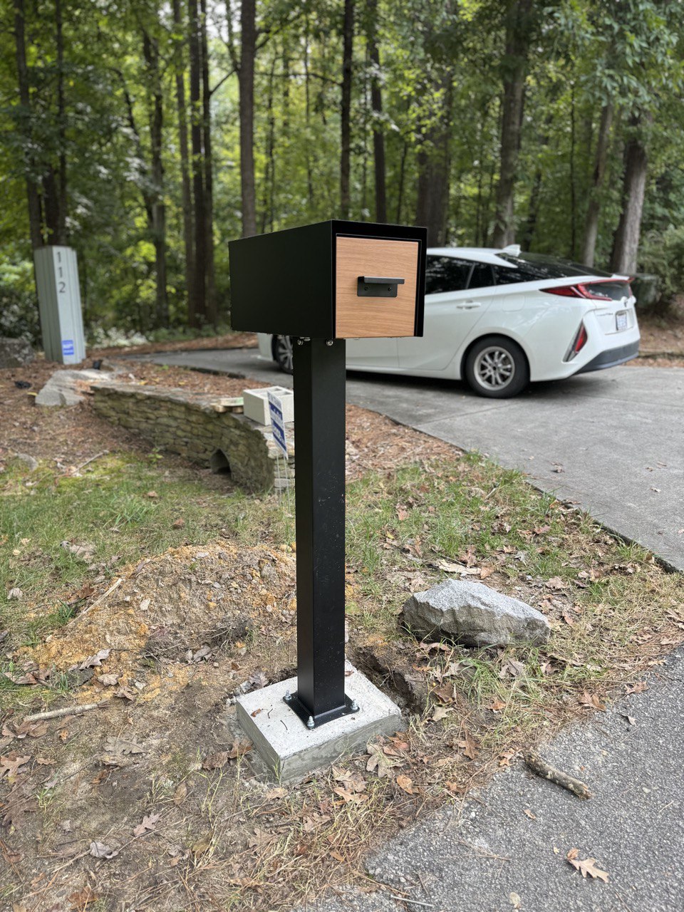 Modern black steel mailbox installed on concrete footing post in wooded Chapel Hill NC driveway