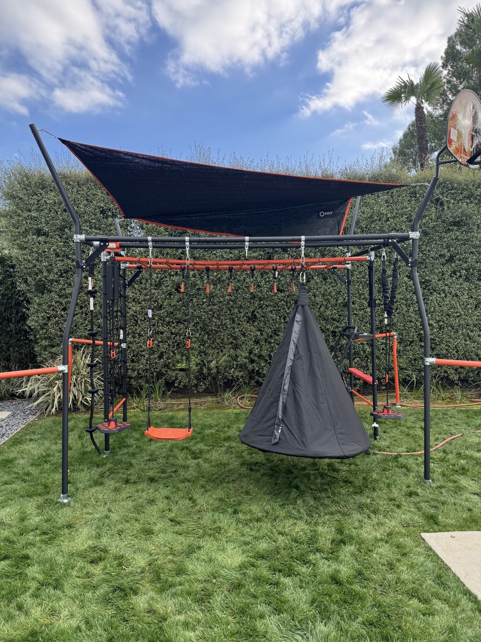Large modular outdoor playset with swings, canopy, and hanging pod assembled in backyard in Triangle NC