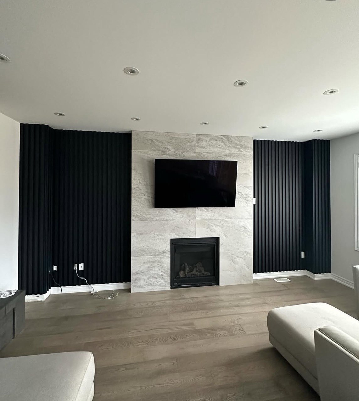 Custom black slat wall panels installed around marble fireplace surround and mounted TV in Triangle NC living room